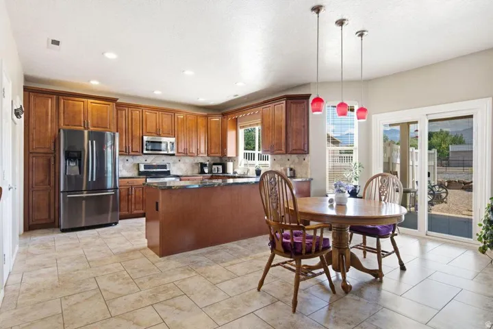 Spacious kitchen featuring warm wood cabinetry, stainless steel appliances, a large island with a stone countertop, recessed lighting, and tile flooring