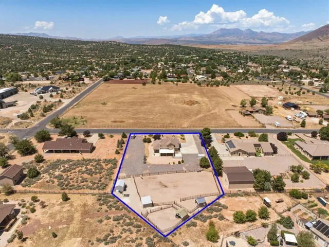 Expansive property featuring a single-story residence with an attached garage, substantial unpaved yard space, multiple outbuildings, and perimeter fencing