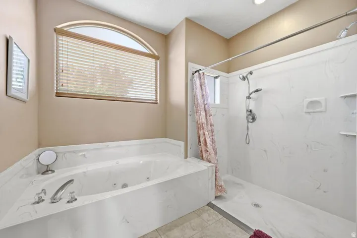 Corner jetted tub with a white composite surround, paired with a walk-in shower featuring a multi-function showerhead and integrated shelving