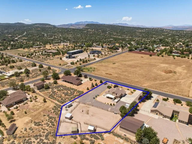 Aerial perspective showcasing a sprawling property featuring a main residence with an attached carport, an extensive unpaved driveway, and a dedicated animal enclosure with multiple shelters