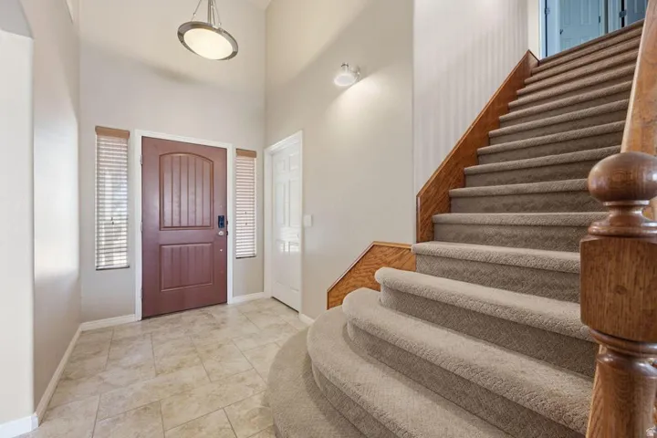 Welcoming foyer featuring a rich burgundy entry door, neutral tile flooring, recessed ceiling lighting, and a curved staircase with wood-finish railings and carpeted treads