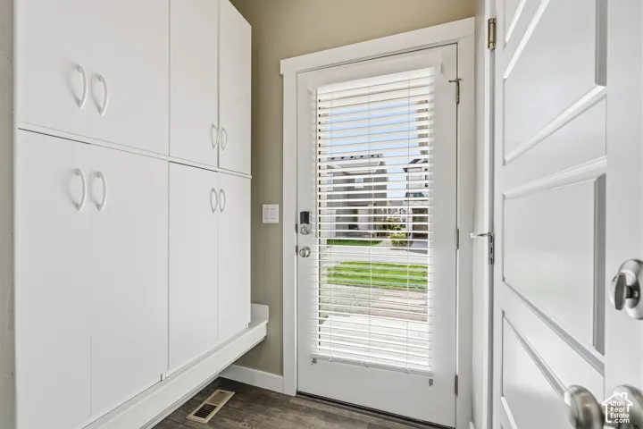 Floor-to-ceiling white cabinetry, integrated bench seating, wood-finish flooring, and a glass-paneled entry door with integrated blinds