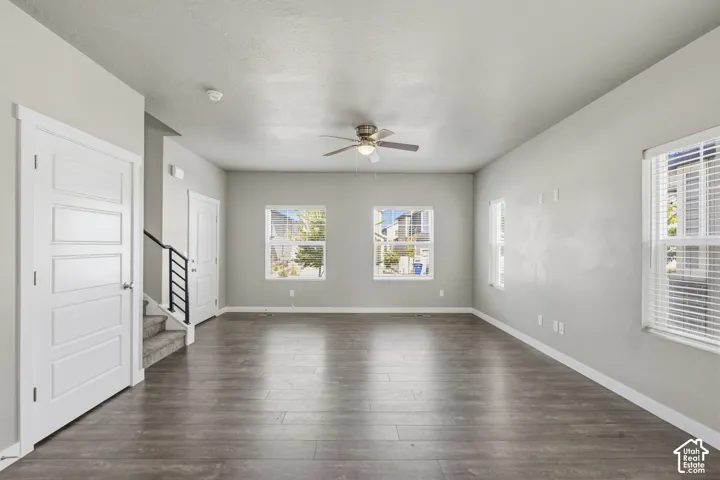 Neutral-toned interior featuring wood-finish flooring, a ceiling fan with integrated light, multiple windows with blinds, and a staircase with a metal railing
