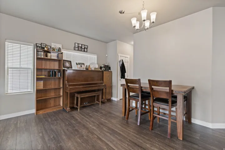 Elegant multi-purpose room showcasing rich wood-finish flooring, a traditional upright piano with bench seating, solid wood dining table with matching chairs, built-in wooden cabinetry with open shelving, and a modern pendant light fixture overhead