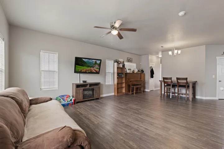 Open-concept living space featuring wood-finish flooring, a ceiling fan with integrated lighting, and multiple windows with blinds