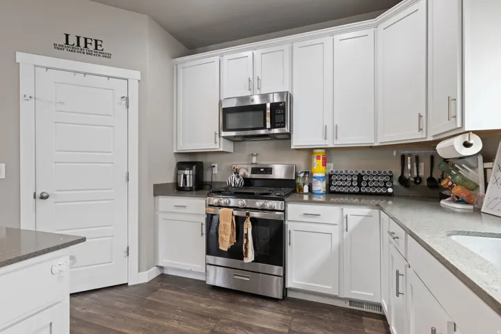 White shaker-style cabinetry, stainless steel appliances, wood-finish flooring, and light-colored countertops