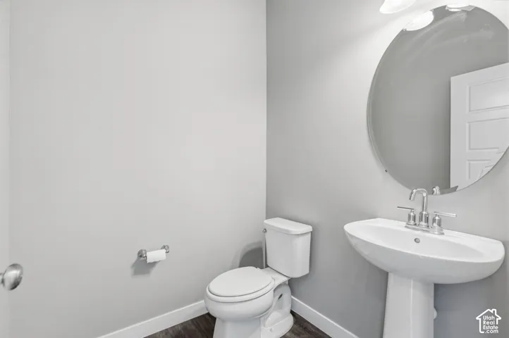 Pedestal sink with a polished chrome faucet, round wall-mounted mirror, and wood-finish flooring