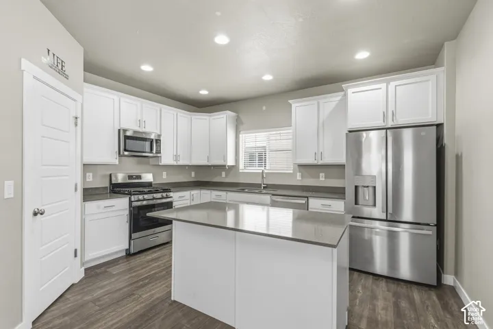 Kitchen featuring white shaker-style cabinetry, a central island with a solid surface countertop, stainless steel appliances, and wood-finish flooring