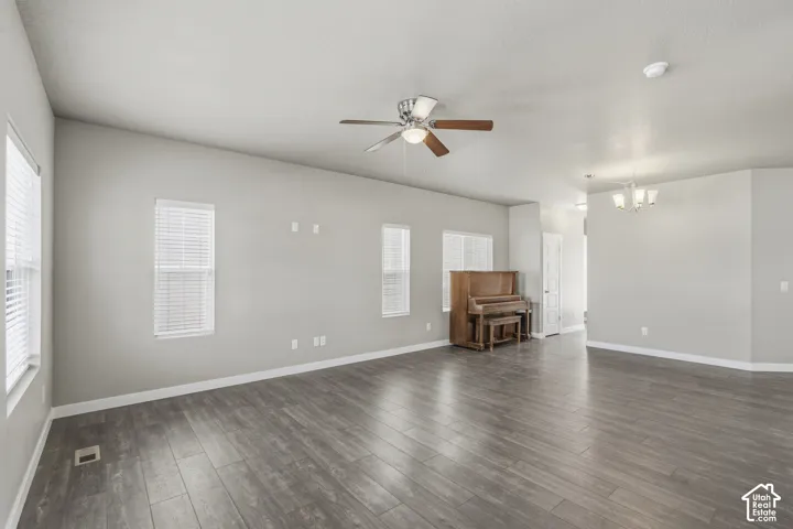 Open-concept interior featuring wood-finish flooring, neutral wall paint, multi-pane windows, a central ceiling fan with integrated lighting, and a multi-arm chandelier