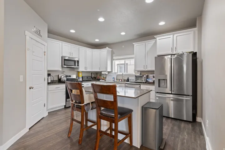 Modern kitchen featuring white cabinetry, stainless steel appliances, an island with countertop seating, recessed lighting, and wood-finish flooring