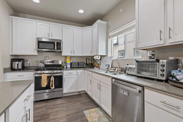 White cabinetry, stainless steel appliances, stone-finish countertops, undermount sink, and wood-finish flooring