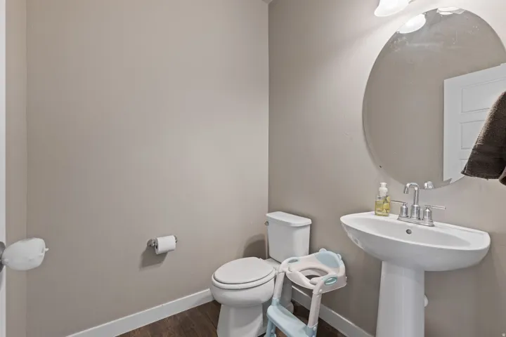 Pedestal sink with chrome fixtures, oval wall mirror, and wood-finish flooring