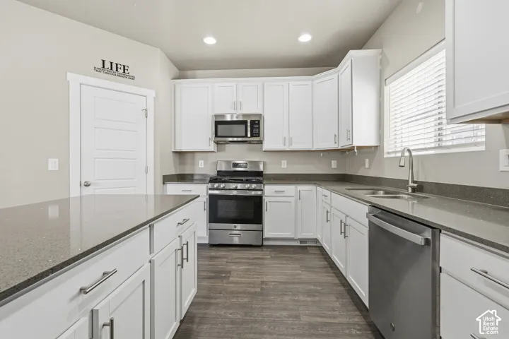 Kitchen featuring white cabinetry, quartz countertops, stainless steel appliances, a center island, and wood-finish flooring