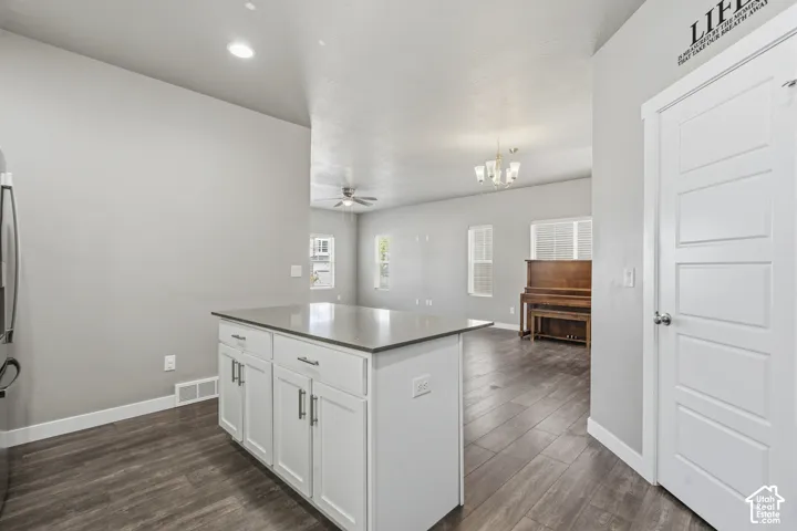 Kitchen island featuring white shaker-style cabinetry, solid-surface countertop, and wood-finish flooring throughout the main level