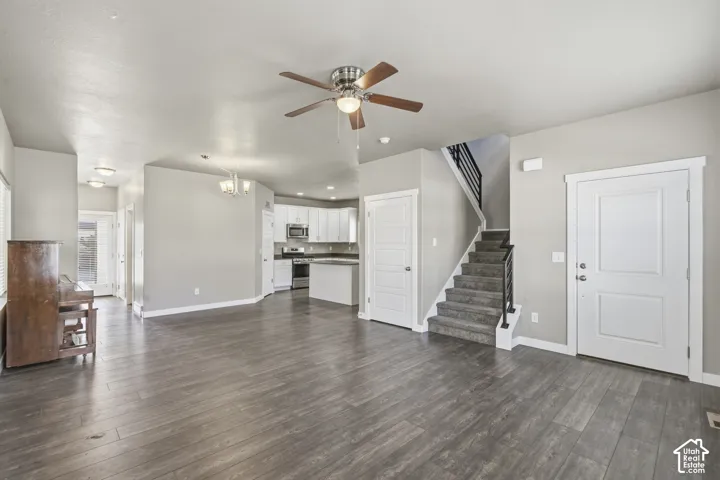 Open-concept floor plan featuring wood-finish flooring, white cabinetry, a kitchen island, recessed lighting, and a staircase with a black metal railing