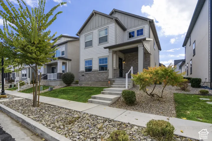 Two-story exterior featuring a mix of horizontal lap and vertical panel siding, stone veneer accents, a covered front porch with a square support column, and concrete entry steps
