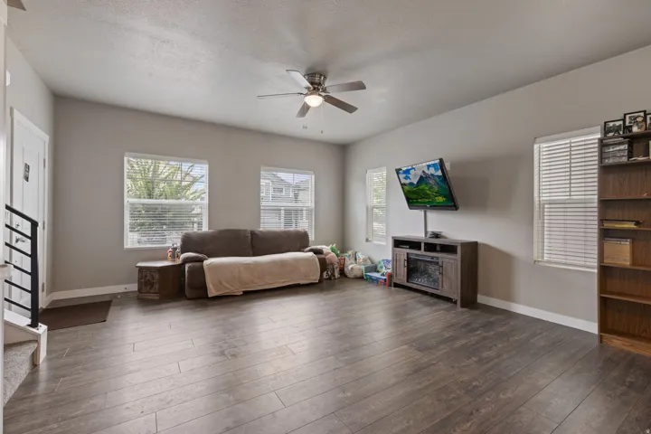 Spacious room with wood-finish flooring, multiple windows with blinds, and a ceiling fan