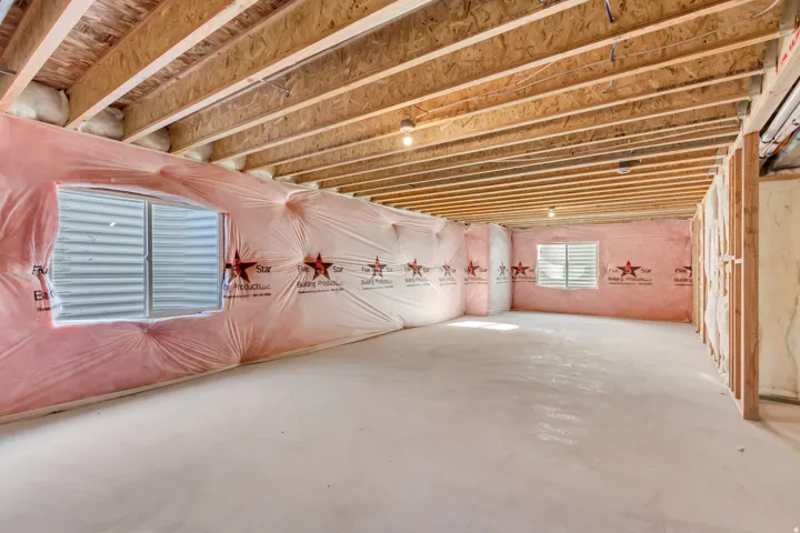 Unfinished basement featuring exposed wood joists and subfloor, insulated walls, concrete flooring, and multiple egress windows