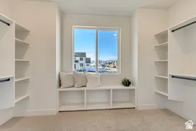 Spacious walk-in closet featuring extensive built-in shelving, hanging rods, and a window seat with integrated storage