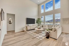 Double-height living space featuring expansive window arrays, light wood-finish flooring, a contemporary black metal stair railing, and neutral wall tones