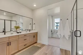 Double vanity with wood-finish cabinetry and white countertops, featuring matte black fixtures and a large frameless mirror