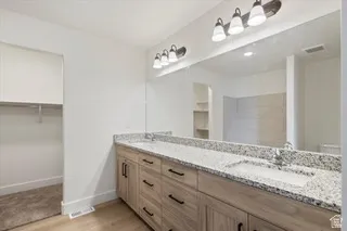 Spa-inspired primary bathroom featuring a dual-sink vanity with warm wood-finish cabinetry, granite countertops, and polished nickel hardware
