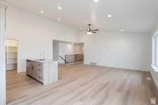 Expansive living area featuring light wood-finish flooring, a kitchen island with a stone-finish countertop, recessed lighting, a ceiling fan, and a built-in pantry with shelving