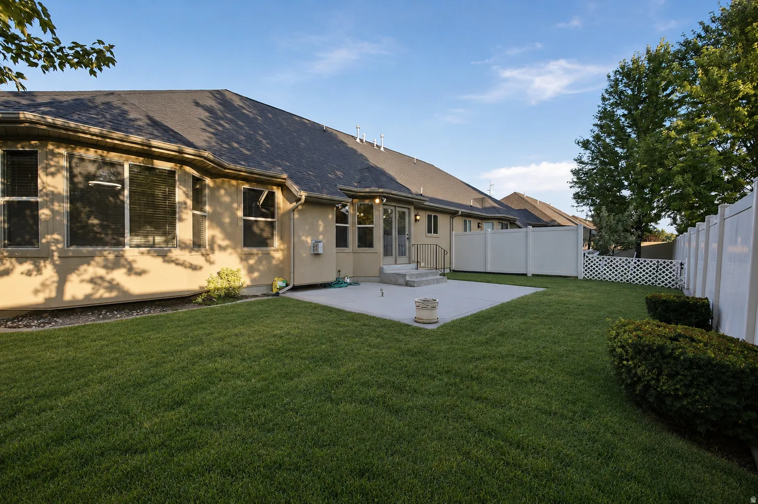 Expansive backyard oasis featuring a manicured lawn, mature landscaping with established trees and shrubs, and a stone patio