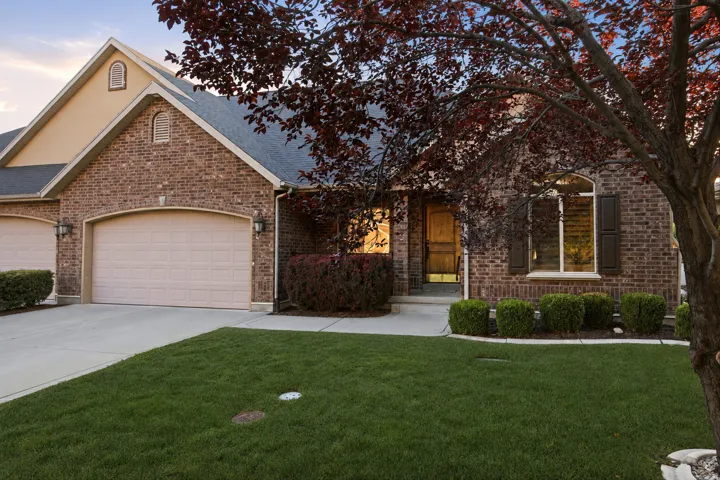 Brick facade residence featuring an attached two-car garage, manicured front lawn, and mature landscaping