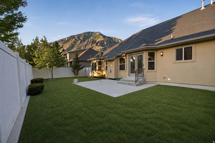 Beautifully landscaped backyard featuring a manicured lawn, mature trees, and a spacious concrete patio