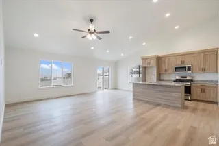 Open-concept living area featuring wood-finish flooring, vaulted ceilings, recessed lighting, a ceiling fan, and a kitchen with stainless steel appliances, a stone countertop, and wood cabinetry