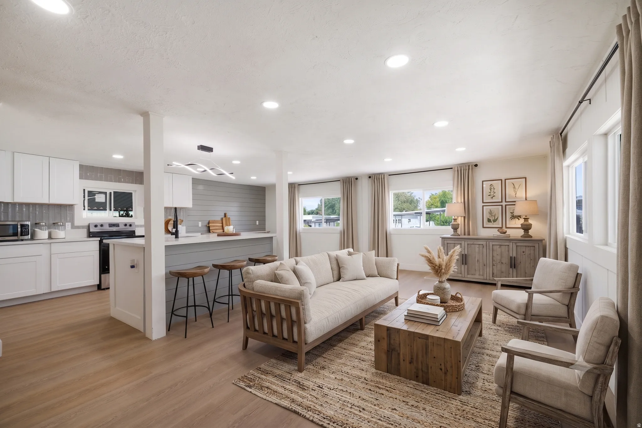 Open-concept living space featuring wood-finish flooring, recessed lighting, and a kitchen with white cabinetry and a breakfast bar