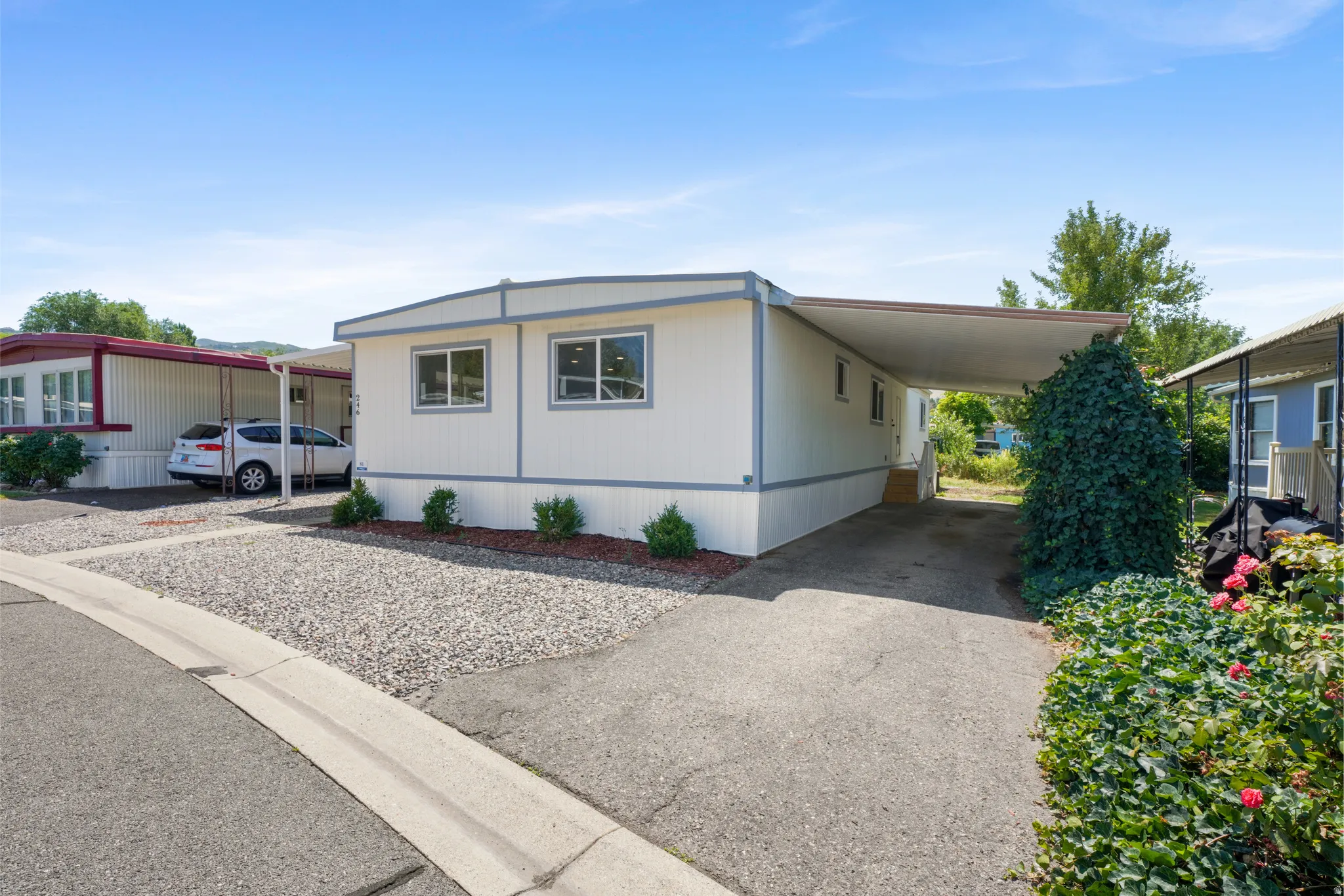 White exterior with gray trim, featuring multiple windows and a covered carport