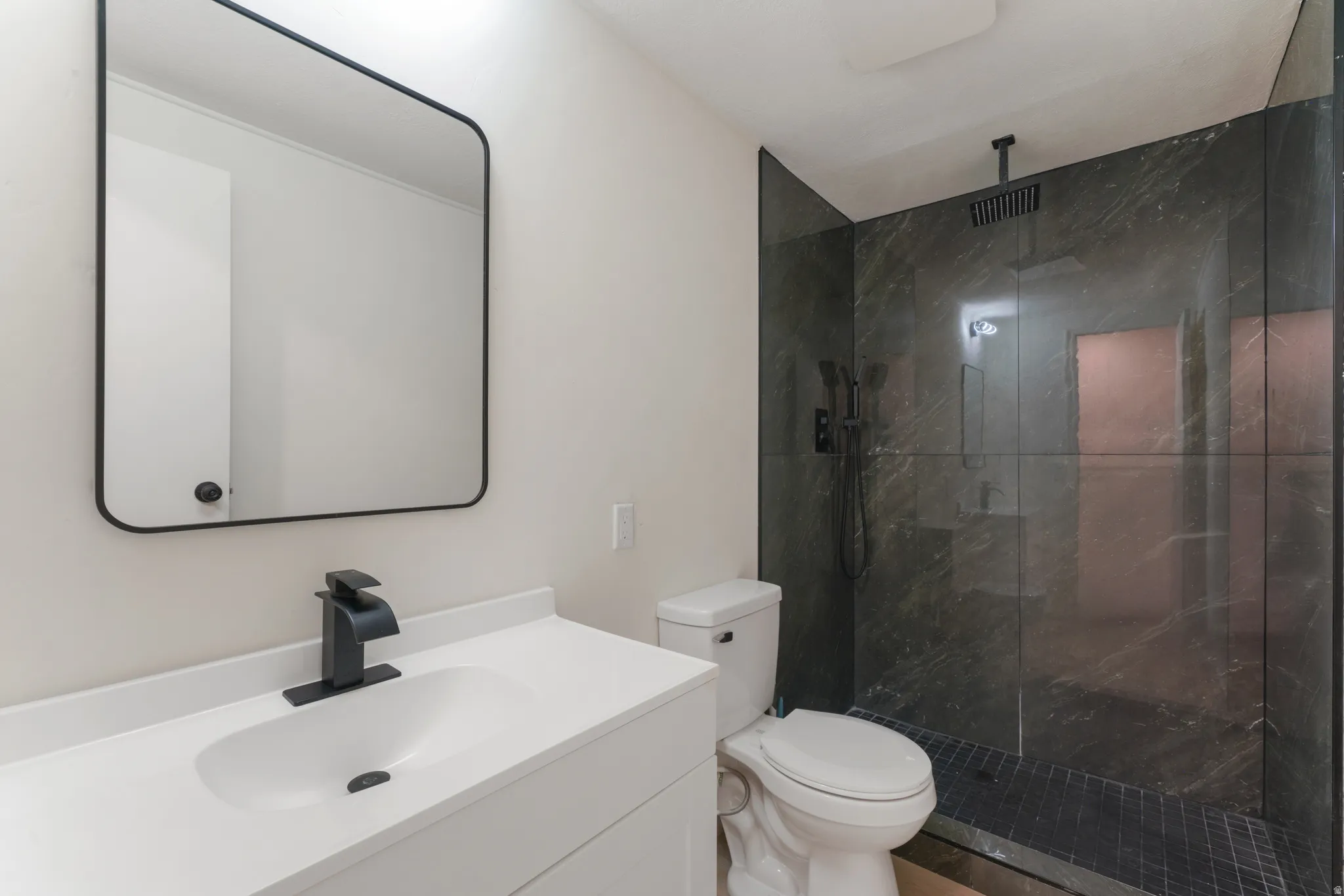 Bathroom featuring a white vanity with an integrated sink, a rectangular black-framed mirror, and a toilet