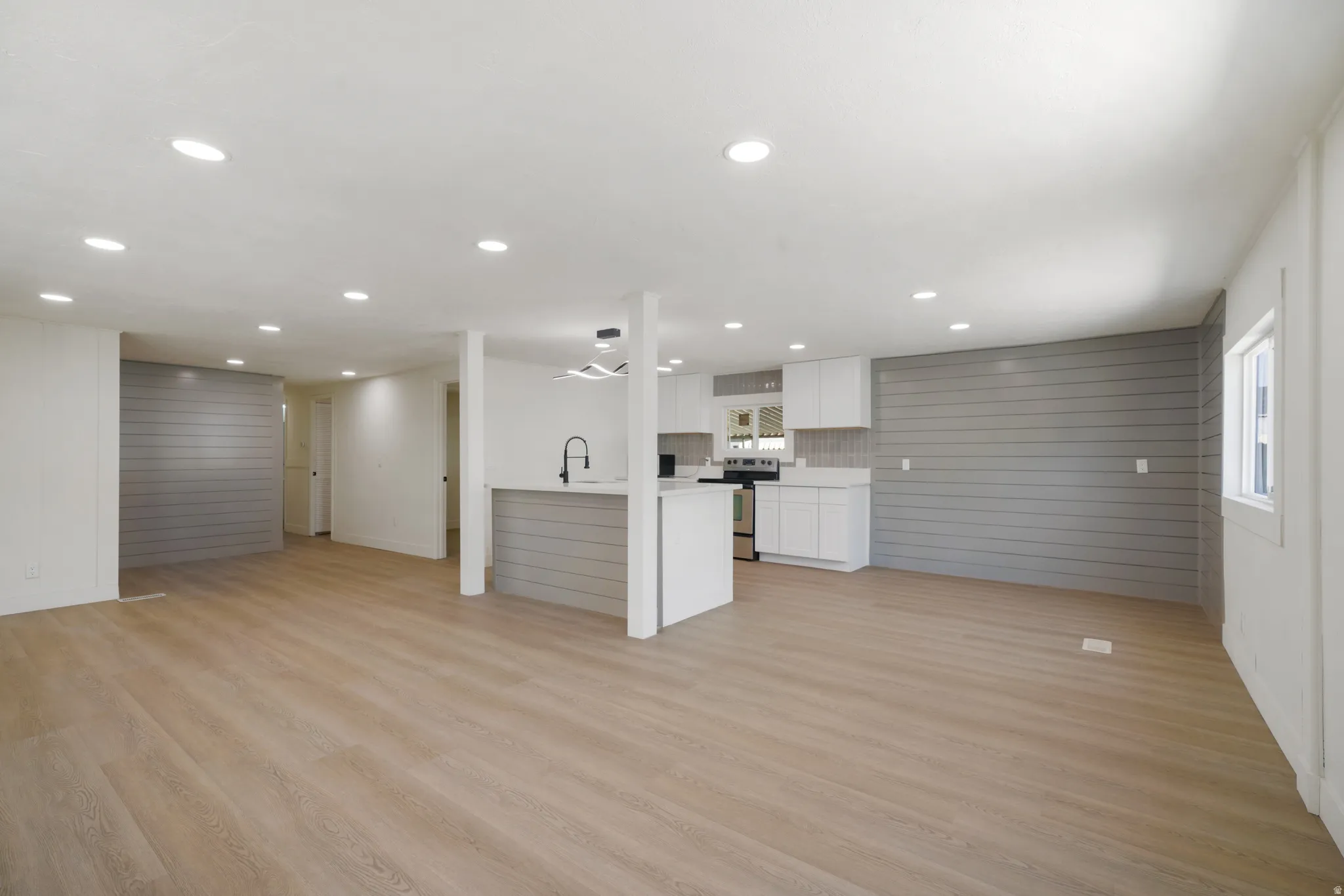 Open-concept living area featuring wood-finish flooring, recessed lighting, and a kitchen with white cabinetry