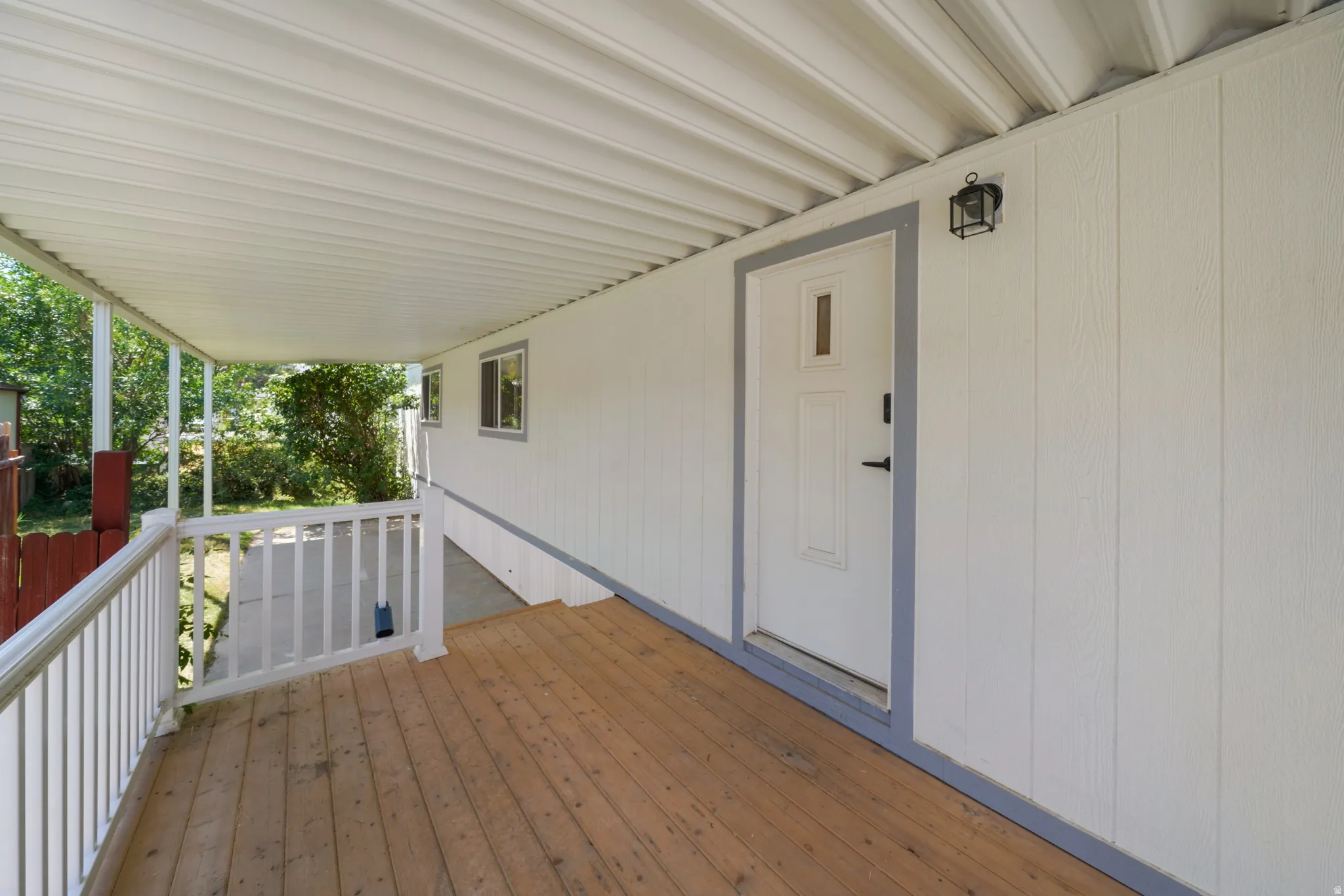 Covered porch featuring wood-finish decking, white railings, and a side-lite entry door
