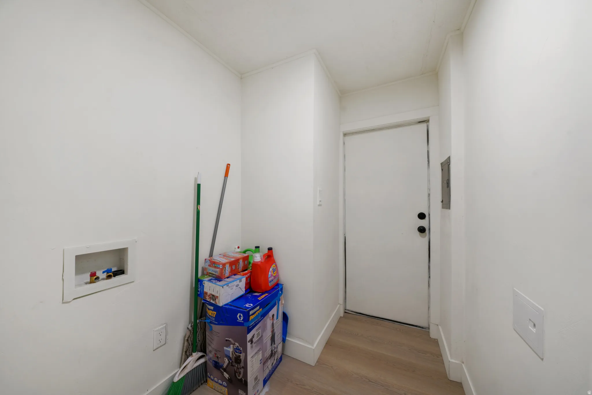 Utility area featuring light wood-finish flooring, white baseboards, and a white interior door with black hardware
