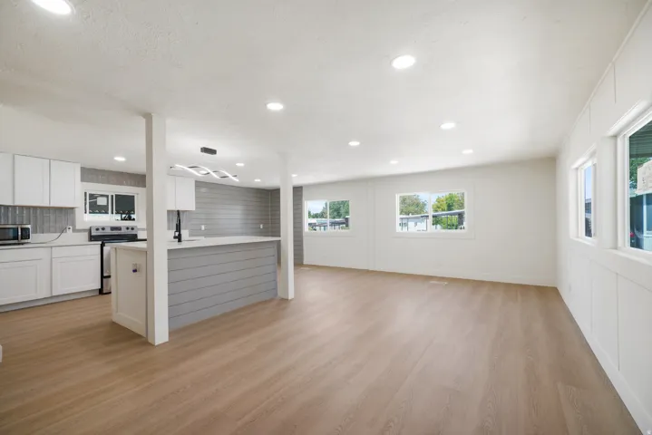 Open-concept living area featuring wood-finish flooring, recessed lighting, white cabinetry, a kitchen island with shiplap detailing, and multiple windows providing natural light