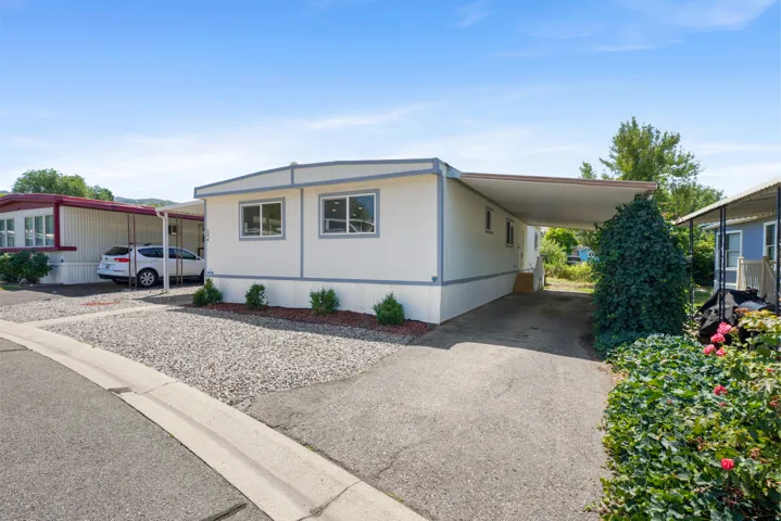White exterior with gray trim, featuring multiple windows and a covered carport