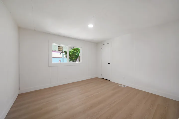 Spacious room featuring light wood-finish flooring, white paneling on walls, a bright window, recessed ceiling lighting, and white baseboards