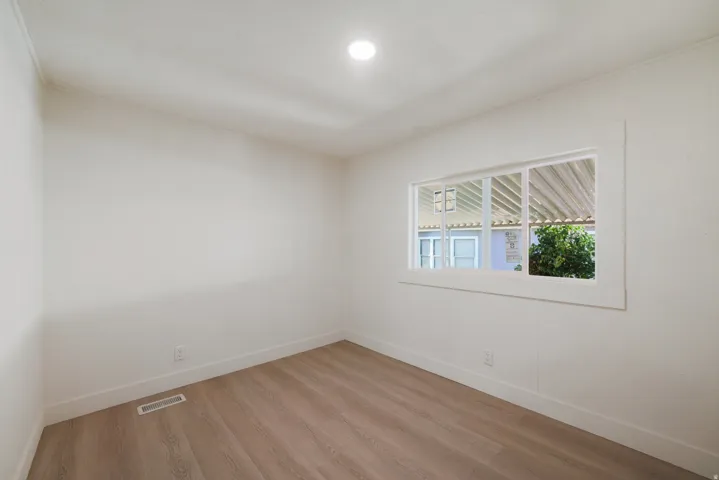 Bright interior room featuring a large window, wood-finish flooring, recessed ceiling lighting, crisp white walls, and clean baseboards