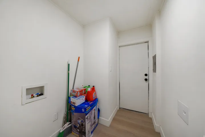 Utility area featuring light wood-finish flooring, white baseboards, and a white interior door with black hardware
