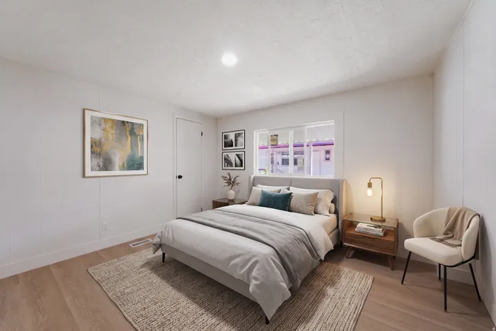 Bedroom featuring light wood-finish flooring, white paneling, and a large window providing natural illumination