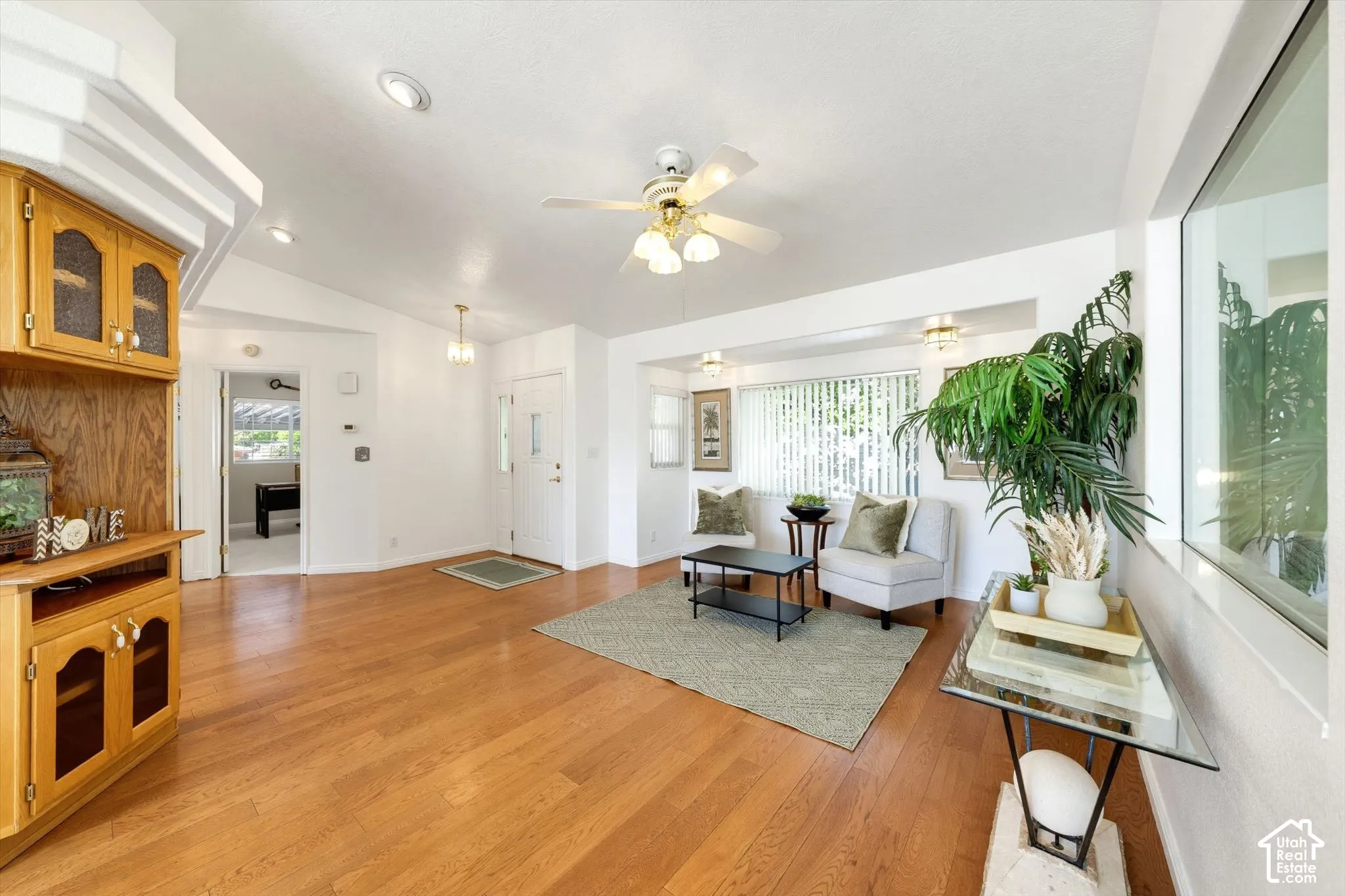 Wood-finish flooring, vaulted ceilings, recessed lighting, built-in cabinetry with glass panel doors, and a ceiling fan with integrated lighting