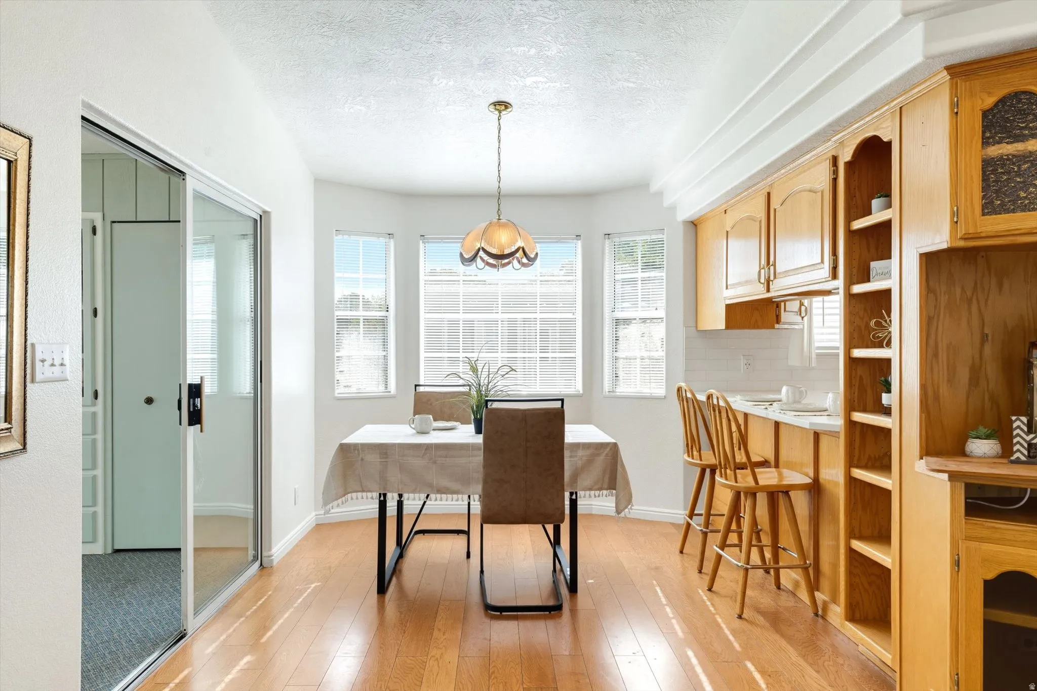 Bay window with multiple panes, wood-finish flooring, built-in cabinetry with open shelving, white subway tile backsplash, and a sliding glass door