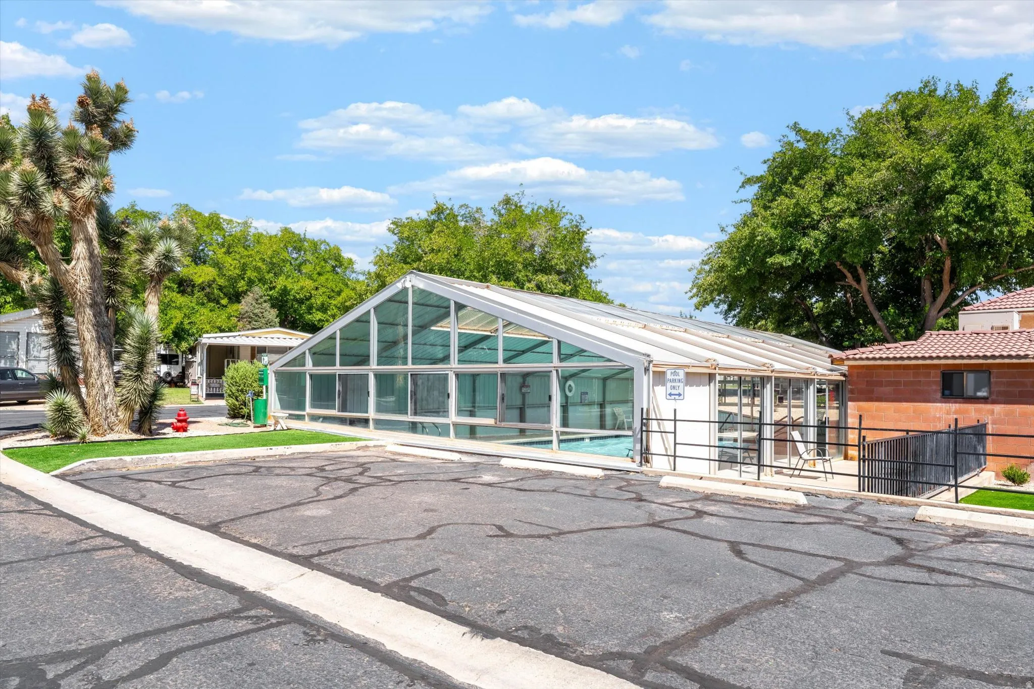 Enclosed swimming pool with a transparent roof, adjacent to a paved parking area