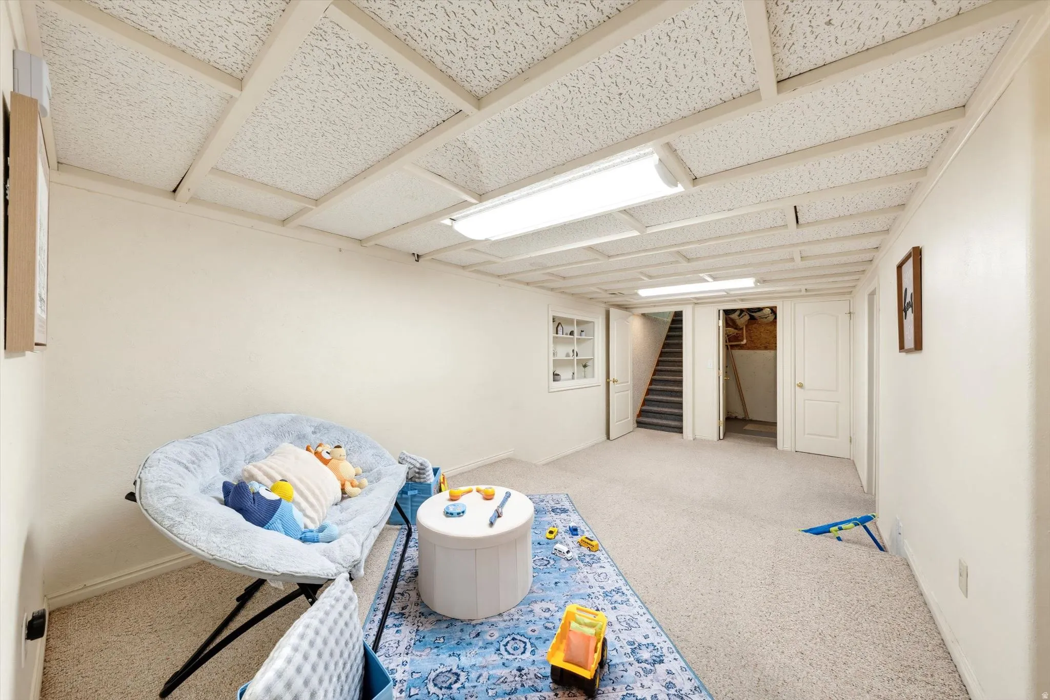 Carpeted flooring, white walls, built-in shelving, two interior doors, and a staircase
