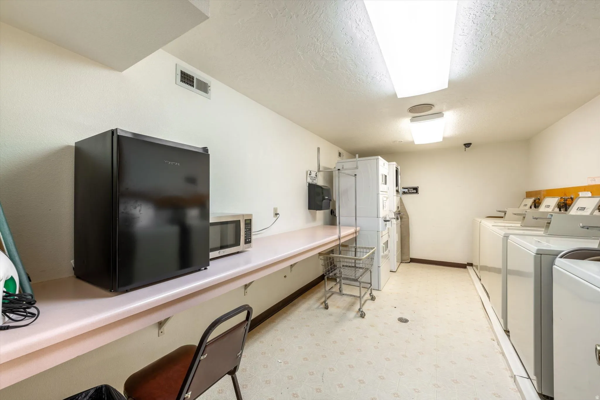 Laundry facility featuring multiple washer and dryer units, a utility counter, and overhead lighting