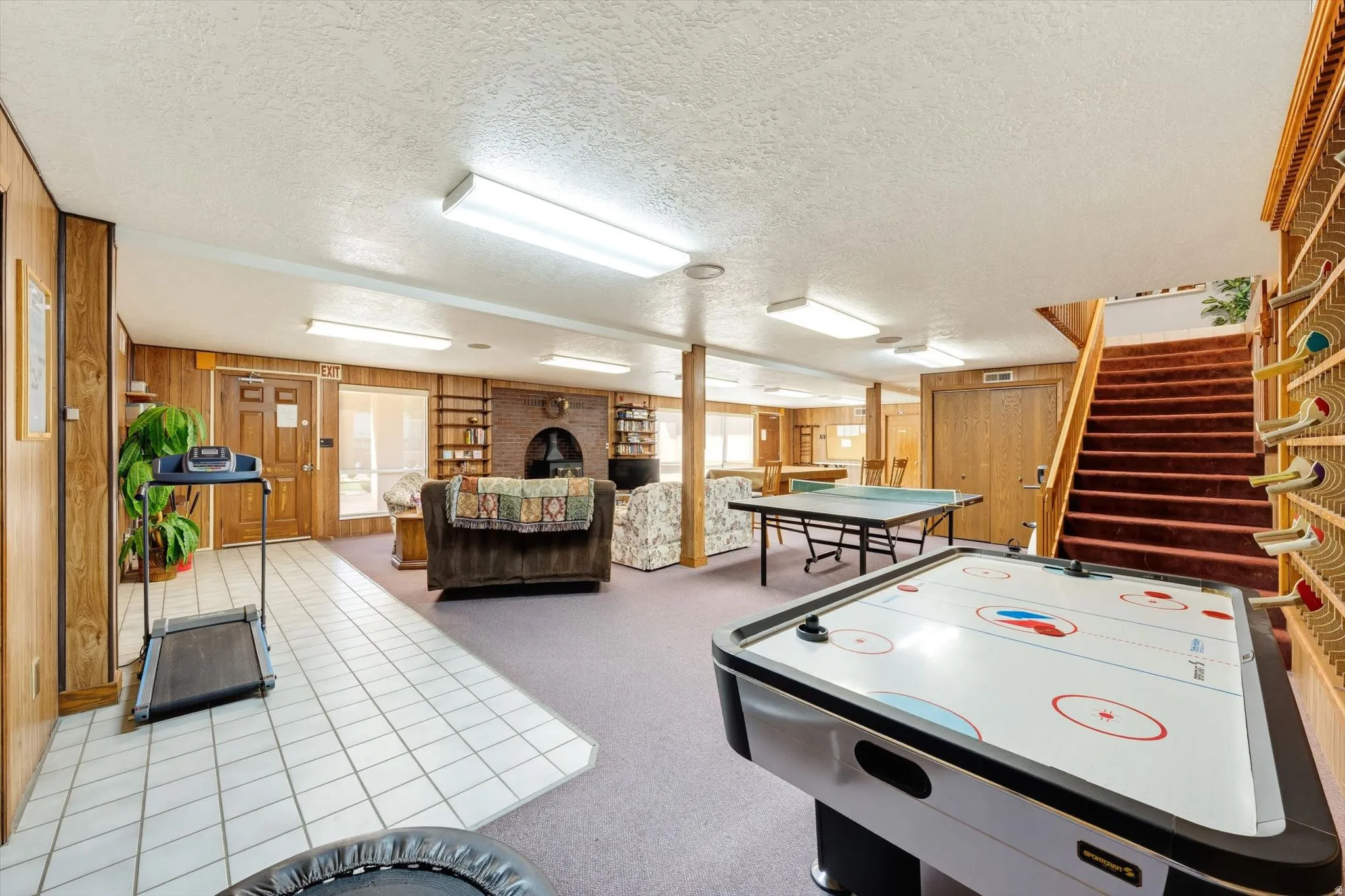 Expansive recreation room featuring wood-paneled walls, a brick fireplace, and a built-in shelving unit