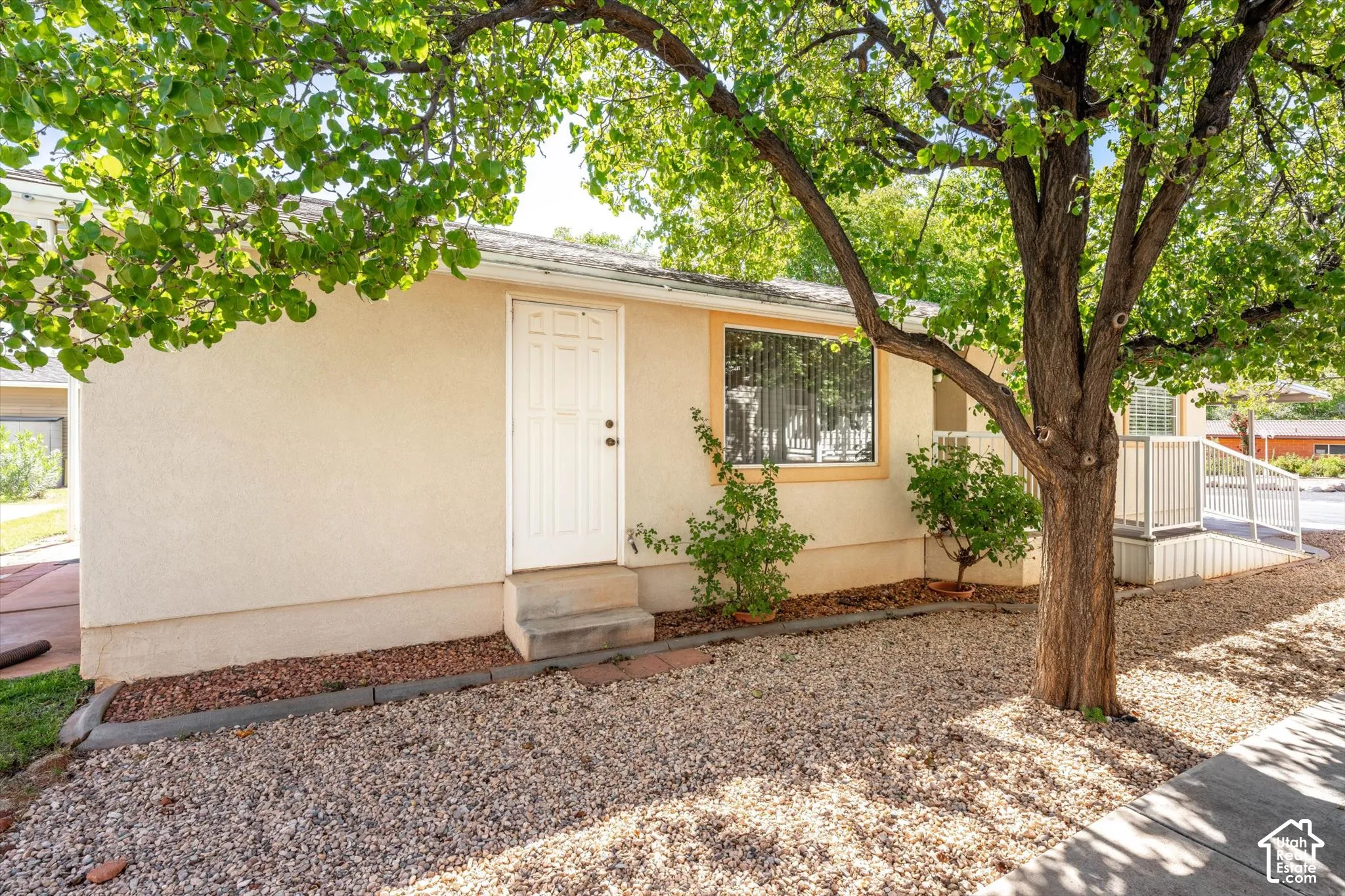 Stucco exterior with a security screen door, an accessible ramp, and a mature tree providing shade